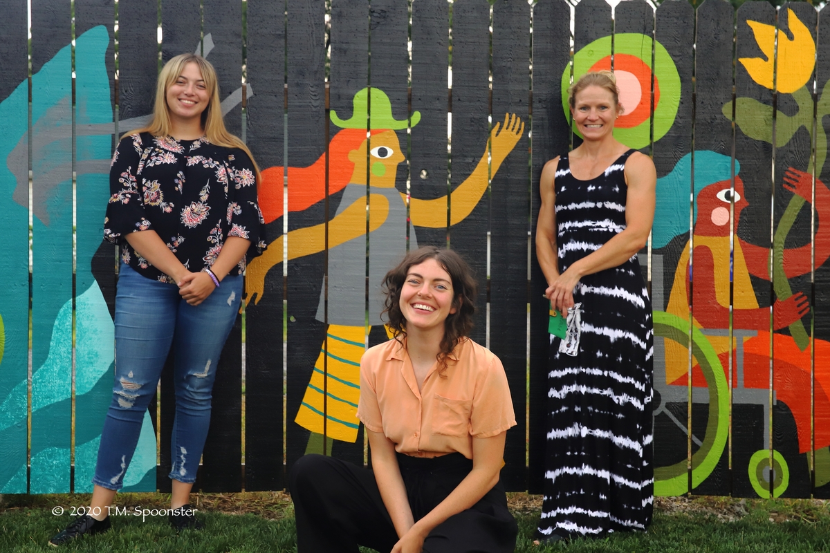 Three people in front of fence mural